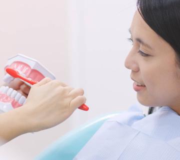 dentist showing woman how to brush with whitening toothpaste