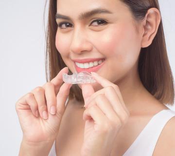 Young smiling woman holding invisalign braces