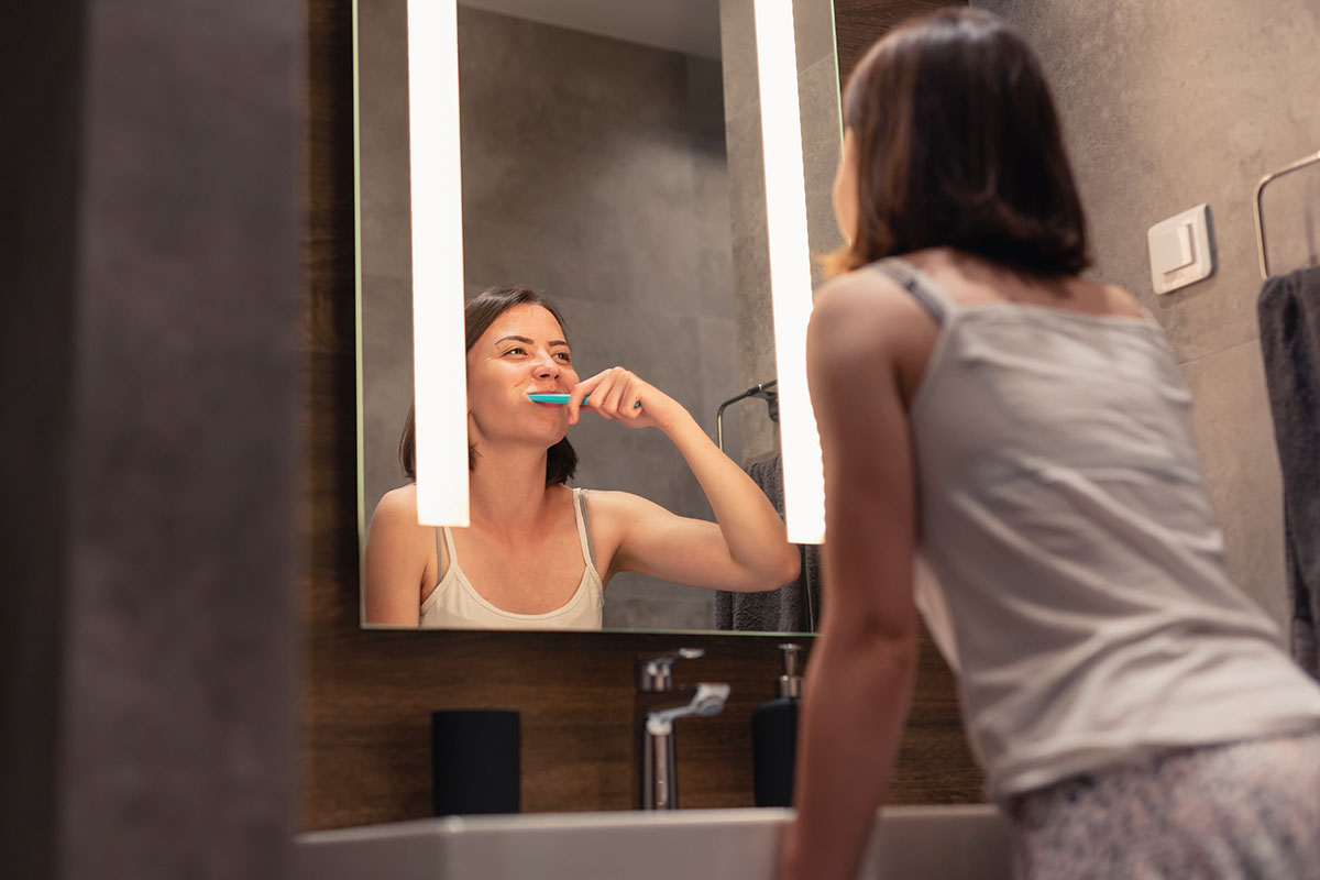 Woman brushing teeth next to bathroom sink